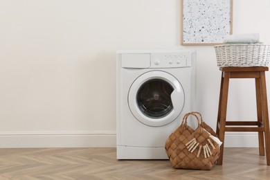 Laundry room interior with modern washing machine and wooden stool near white wall. Space for text