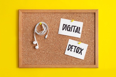 Corkboard with words DIGITAL DETOX and earphones hanging on yellow background