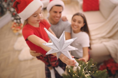 Family decorating Christmas tree indoors, focus on star topper