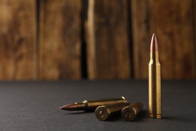 Bullets on black table against wooden background, closeup. Space for text