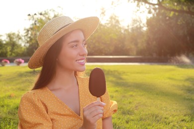 Beautiful young woman holding ice cream glazed in chocolate outdoors, space for text