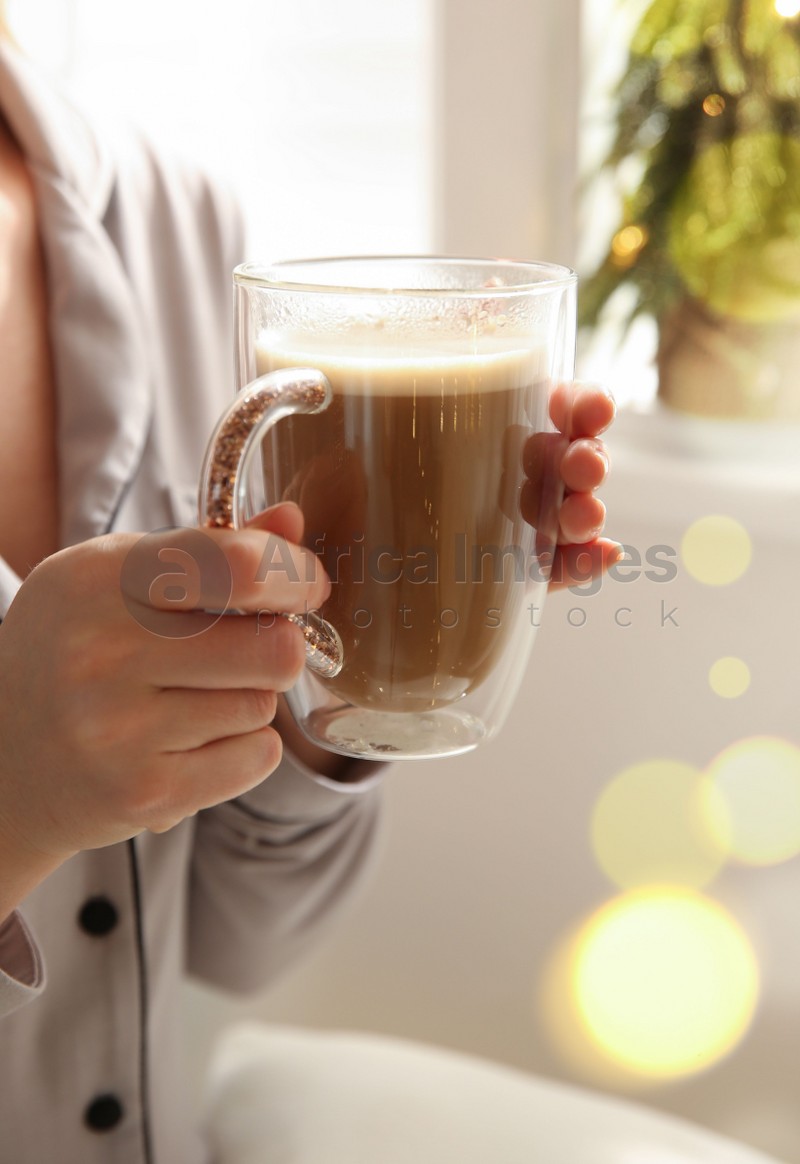 Woman holding cup with hot drink indoors, closeup