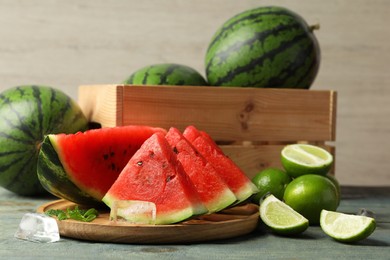 Slices of delicious watermelon, limes, ice and mint on light blue wooden table