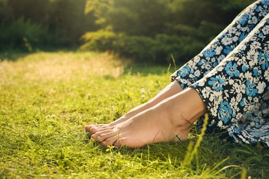 Woman relaxing barefoot on green grass, closeup. Space for text