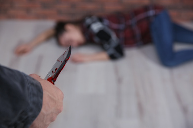 Man with bloody knife and his victim on floor indoors, closeup. Dangerous criminal