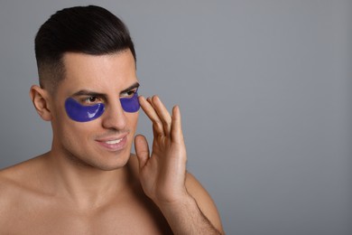 Man applying blue under eye patch on grey background. Space for text