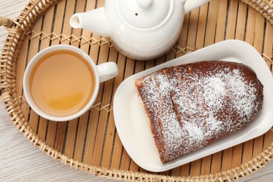 Photo of Delicious yeast dough cake and tea on wicker tray, top view