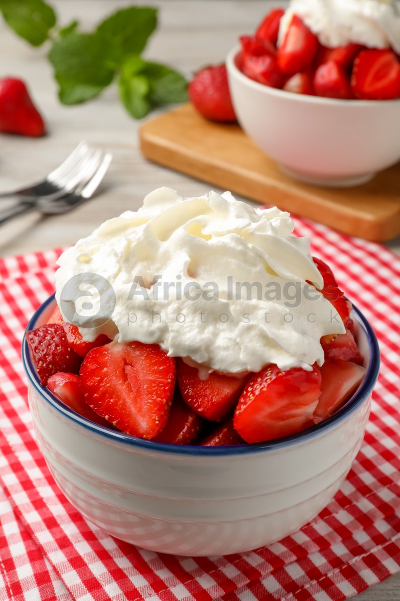 Bowl with delicious strawberries and whipped cream served on table, closeup