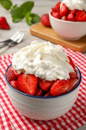 Photo of Bowl with delicious strawberries and whipped cream served on table, closeup