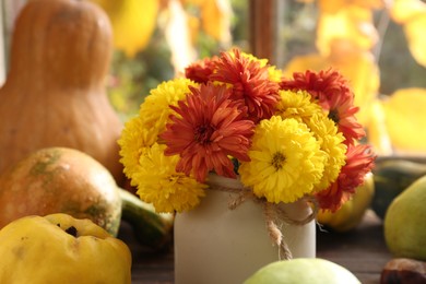 Photo of Beautiful colorful chrysanthemum flowers in vase and pumpkins indoors, closeup. Autumn still life