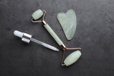Quartz gua sha tool, face rollers and dropper with cosmetic product on grey background, flat lay