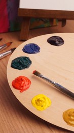 Photo of Artist's palette with samples of colorful paints and brush on wooden table