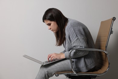Young woman with bad posture using laptop while sitting on chair against grey background