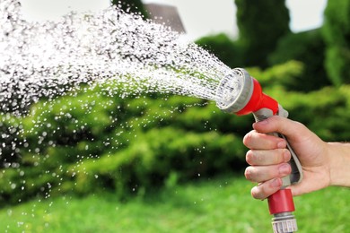 Photo of Man spraying water from hose in garden, closeup