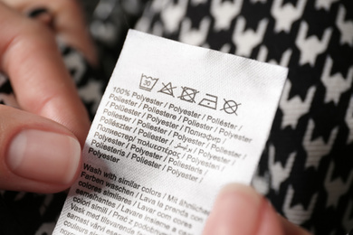Woman reading clothing label with care symbols and material content on shirt, closeup