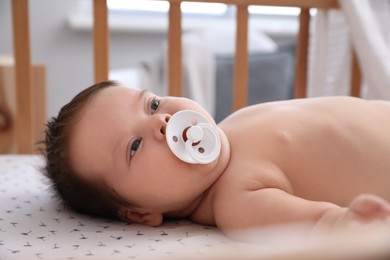 Cute little baby with pacifier lying in comfortable crib at home. Bedtime