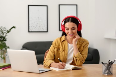 Photo of Online translation course. Student in headphones writing near laptop at home