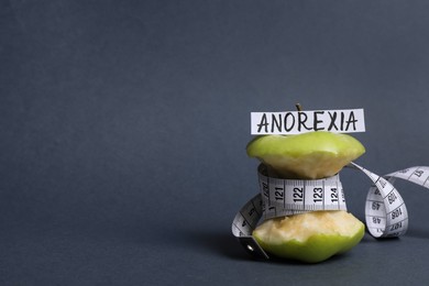 Apple core with measuring tape and word Anorexia on dark grey background, space for text
