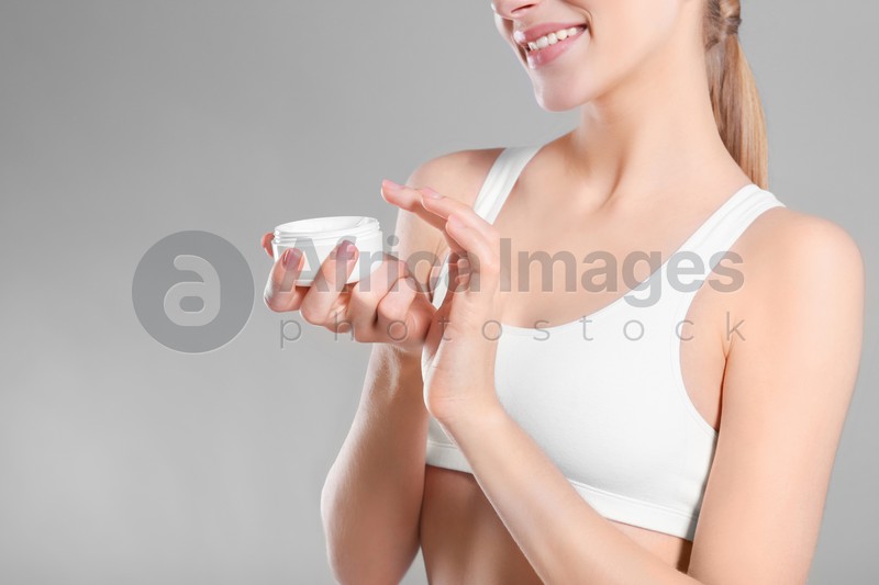 Young woman with jar of body cream on color background
