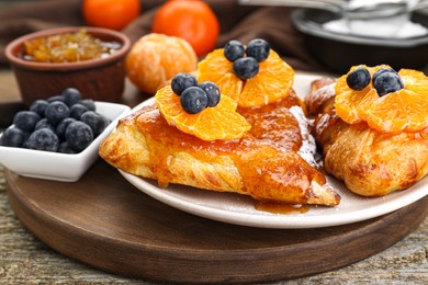 Photo of Fresh tasty puff pastry with sugar powder, jam, tangerines and blueberries on wooden table, closeup