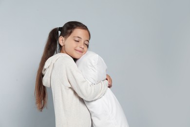 Cute girl in white pajamas hugging pillow on light grey background. Space for text