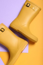 Pair of yellow rubber boots on color background, top view