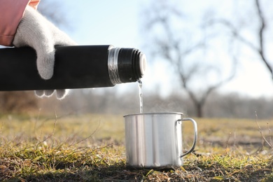 Photo of Woman pouring hot drink into mug from thermos outdoors, closeup