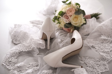 Pair of white high heel shoes, veil and wedding bouquet on grey background