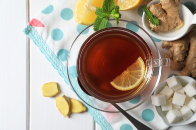 Photo of Cup of delicious ginger tea, sugar cubes and lemons on white wooden table, flat lay