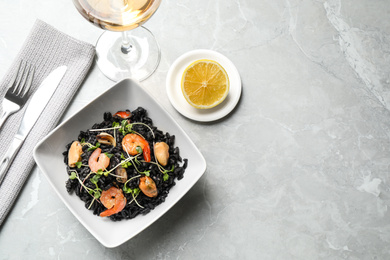 Photo of Delicious black risotto with seafood served on light grey marble table. Space for text