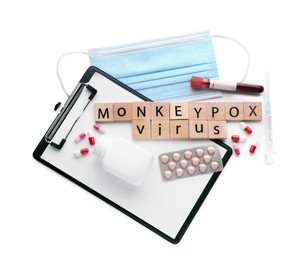 Photo of Words Monkeypox Virus made of wooden cubes, test tube, medical face mask, different pills, syringe and clipboard on white background, top view