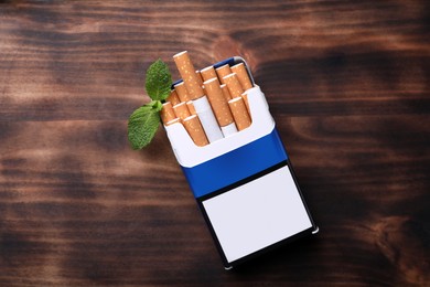 Pack of menthol cigarettes and mint leaves on wooden table, flat lay