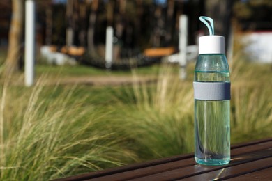 Glass bottle with water on wooden surface outdoors. Space for text