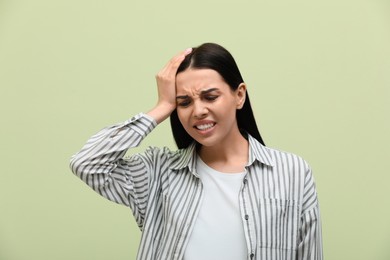 Woman suffering from migraine on light green background