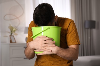 Young man with bucket suffering from nausea at home. Food poisoning