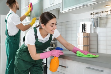 Portrait of woman cleaning table with rag and her colleague in kitchen