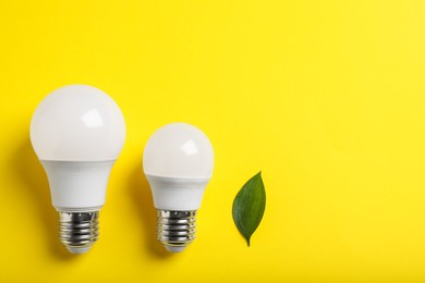 Light bulbs and green leaf on yellow background, flat lay. Space for text