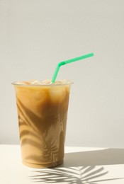 Plastic takeaway cup of delicious iced coffee on white table under sunlight