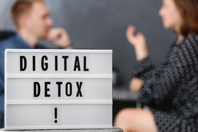 Photo of Colleagues chatting in office, focus on lightbox with phrase DIGITAL DETOX