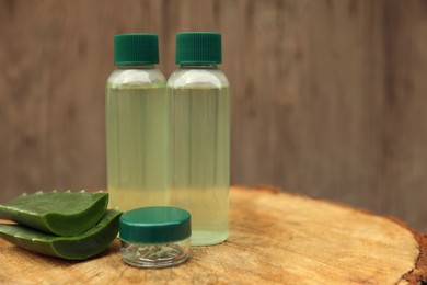 Bottles of cosmetic products and sliced aloe vera leaves on wooden stump. Space for text