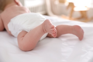 Photo of Cute little baby in diaper on bed, closeup