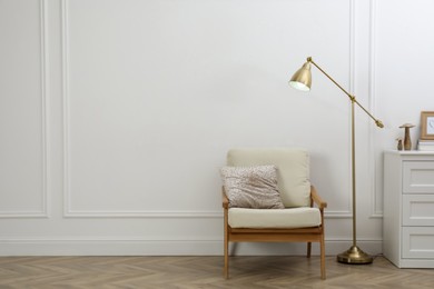 Stylish room interior with lamp, chest of drawers and armchair near white wall. Space for text