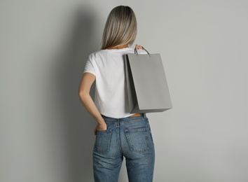 Woman with paper shopping bag on light grey background, back view
