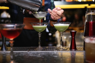 Bartender pouring tasty cocktail at counter in nightclub, closeup