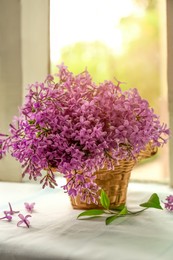 Beautiful lilac flowers in wicker basket on window sill indoors