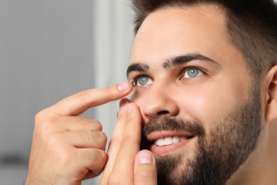Closeup view of young man putting in contact lens on blurred background