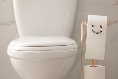 Modern toilet bowl and paper with funny face in bathroom