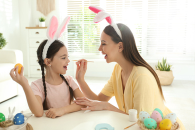 Happy mother and daughter with bunny ears headbands having fun while painting Easter egg at home