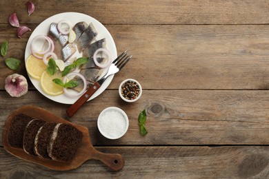 Photo of Sliced salted herring fillet served with basil, onion rings and lemon on wooden table, flat lay. Space for text