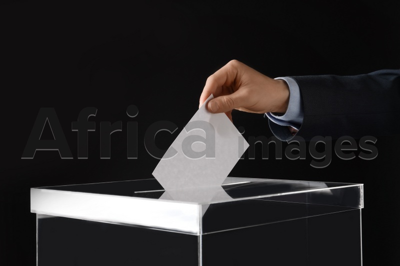 Man putting his vote into ballot box on black background, closeup